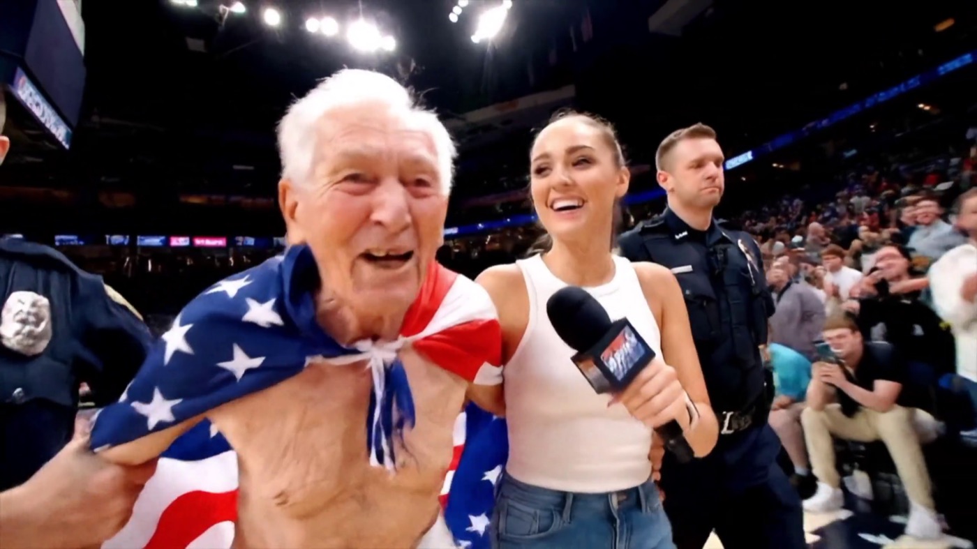An AI-generated frame of an older man draped in an American flag shouting into a reporter's microphone next to a police officer on an NBA arena court, with a caption reading IND wins Championship $1,000 to $1,173